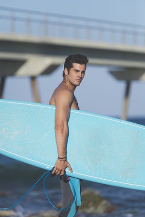 Male surfer with board standing on sunny coastline