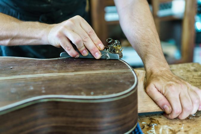 Male hands shaving back of guitar in luthier workshop