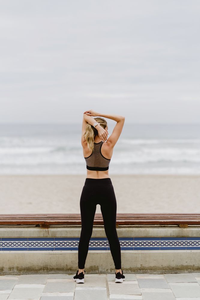 Faceless female gymnast in sports clothing stretching before exercise at seaside