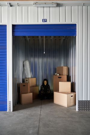 Young woman inside a warehouse to store moving boxes organizing with her laptop