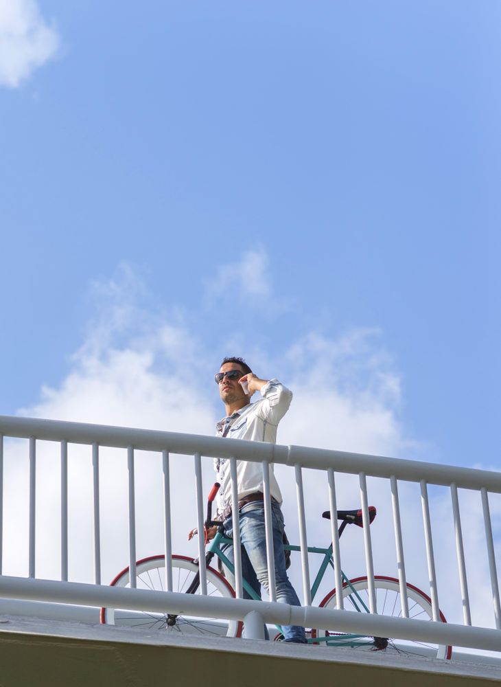 Looking up at male on bike on bridge using phone