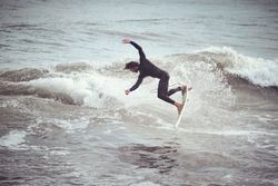 Surfer male jumping on wave standing on surfboard in ocean