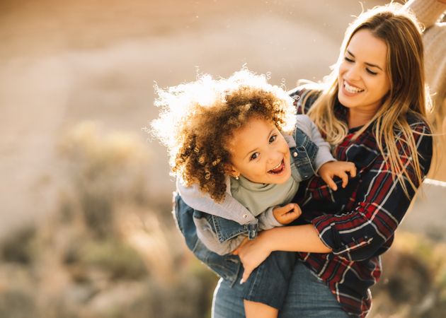 Cheerful woman play with toddler on nature