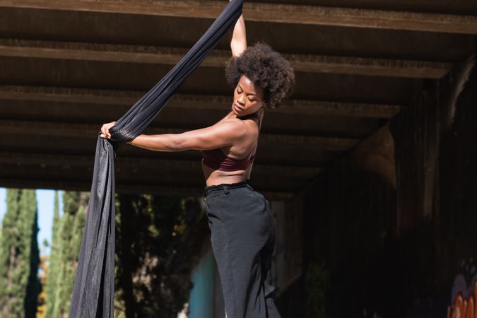 Black woman doing yoga with aerial silks in city