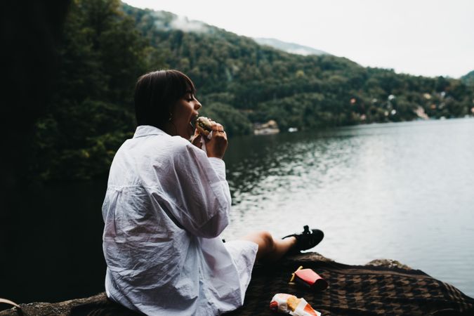Woman eating hamburger near lake and mountains