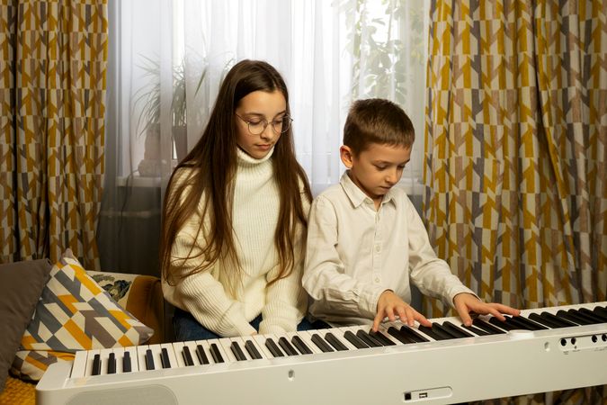 Boy in white shirt plays piano while girl observes.