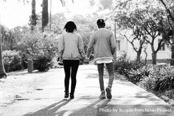Back view of man and woman holding hands and walking on sidewalk in grayscale 4AwkY0