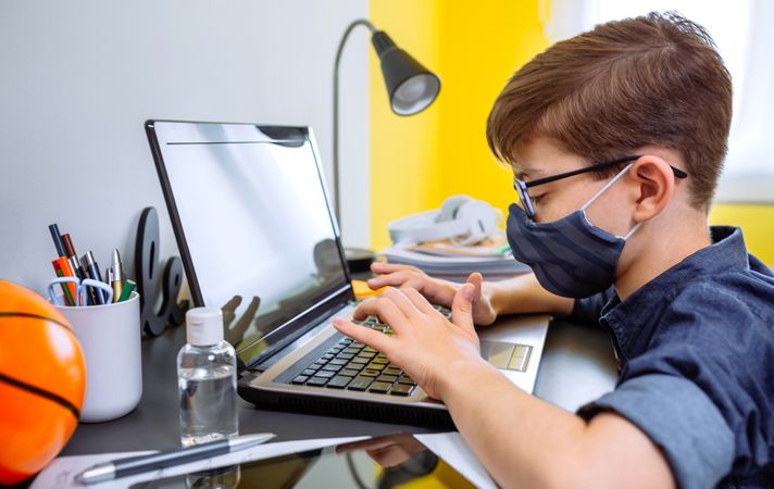 Teenager with face mask doing homework with laptop