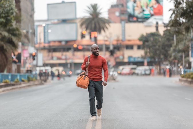 Man in red shirt holding bag walking on street