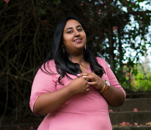 Portrait of woman wearing pink shirt standing near trees