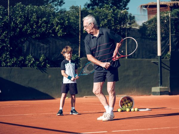 Male tennis instructor teaching preteen boy on hard court