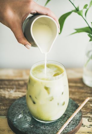 Iced matcha drink with hand pouring cream from pitcher, close up
