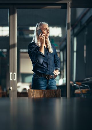 Mature businesswoman standing in boardroom talking on mobile phone
