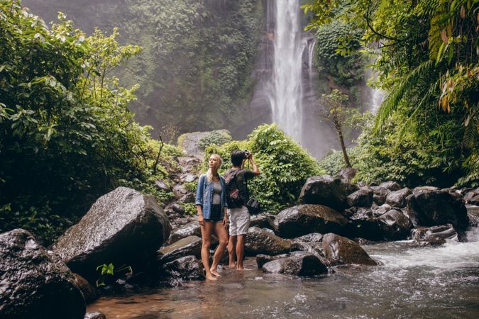 Friends standing in creek in front of tropical waterfall