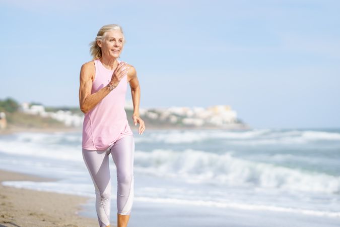 Mature woman in sports gear jogging along beach