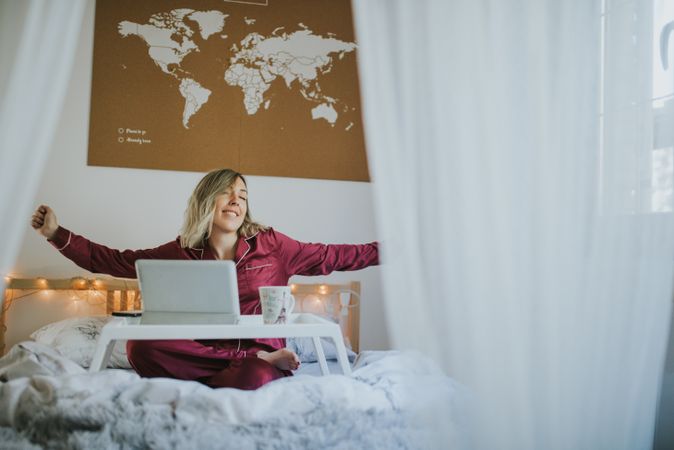 Woman stretching in bed with laptop