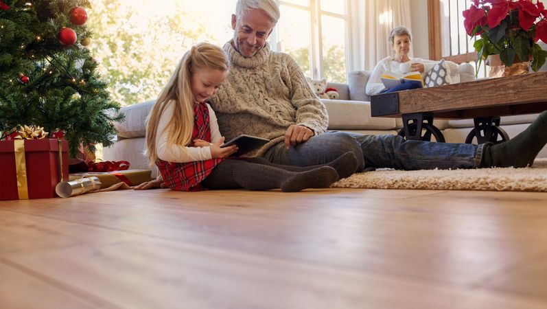 Grey haired man with granddaughter using digital tablet at home