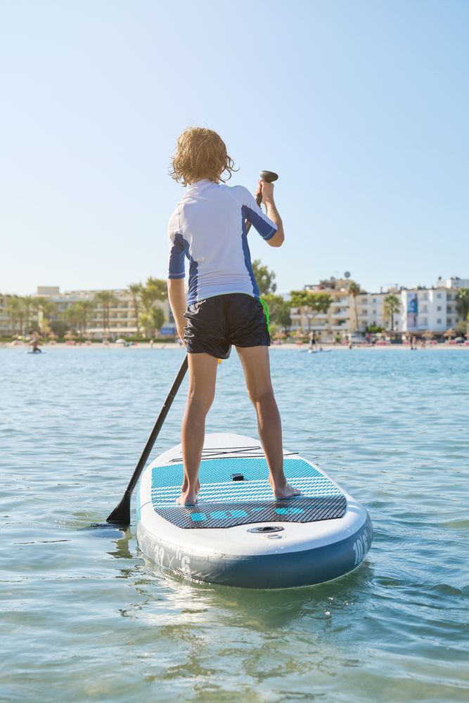 Anonymous child on paddleboard in ocean during summer day