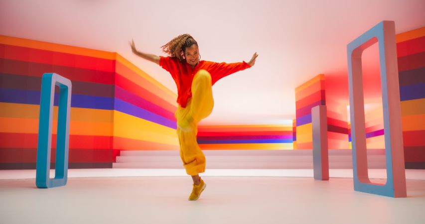Portrait of a Talented Black Female Artist Showcasing Energetic Dance Movements in Abstract Colorful Studio Decoration.