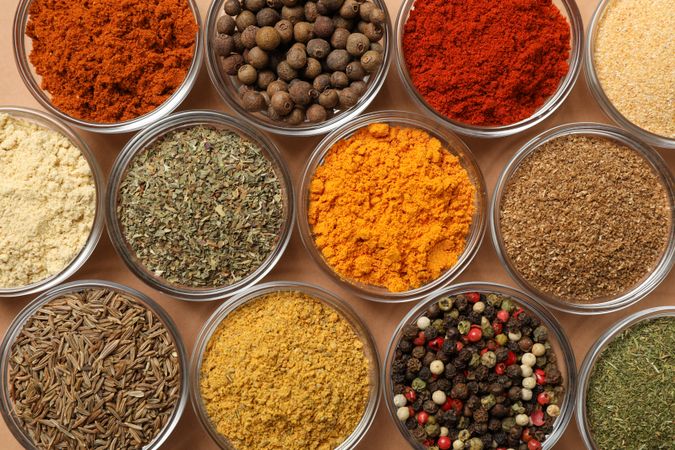 Top view of bowls of spices in rows on beige table