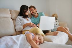 Smiling mother and father watching video on laptop near sleeping