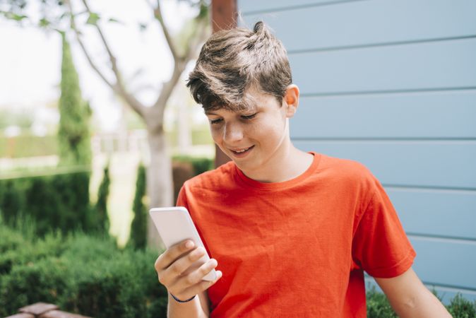 Teenage boy standing outside wearing red t-shirt using phone