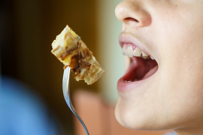 Mouth of girl eating bite of fritata