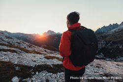Back view of man in red jacket with backpack gazing the horizon in the mountains at sunset 4OJQ75