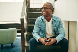 Portrait of smiling man in jean jacket on stairwell with cellphone