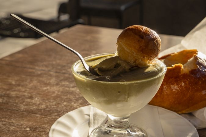 Sicilian pistachio granita with brioche dipped into glass cup at outdoor breakfast table