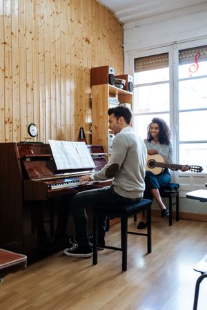 Man playing piano near woman playing guitar in studio