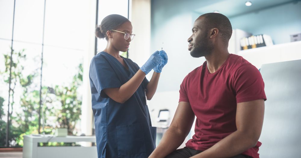 Black Female Nurse Is Performing Injection And Putting A Patch On.