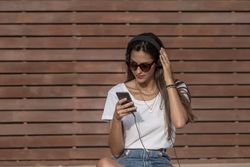 Woman using headphone to listen to music sitting against brown background