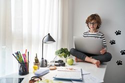 Cheerful boy browsing laptop while sitting on table