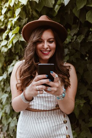 Woman in hat smiling browsing smartphone