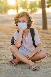 Boy in mask sitting on paved walkway and looking at camera