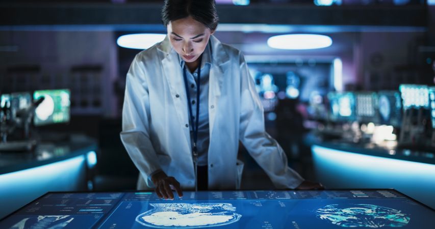 Female Asian Neuroscinetist Using Interactive Touch Screen Table With MRI Scans On Display In Modern Biotechnology Research Center.