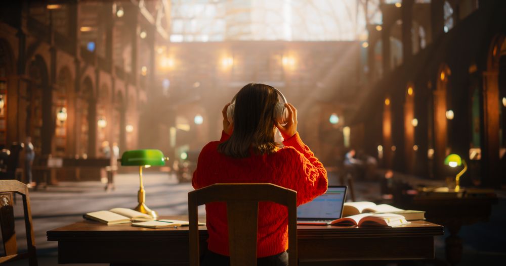 Young Asian Female Student Engrossed in Online Learning With Headphones and Laptop in a Historic Library.