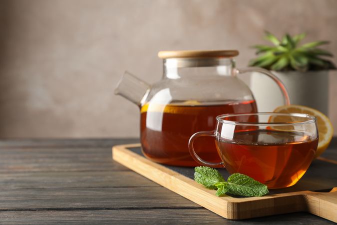 Cup of tea, mint, honey, ginger and teapot on wooden background, space for text