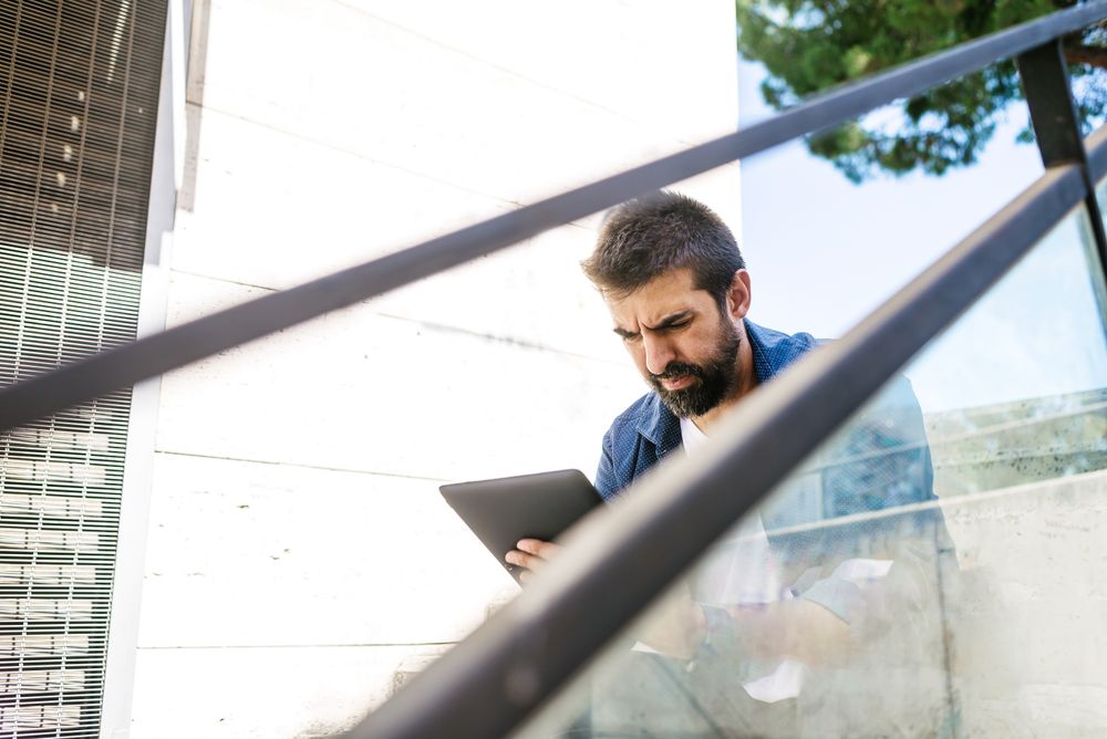 Serious man sitting on stairs checking tablet outdoors