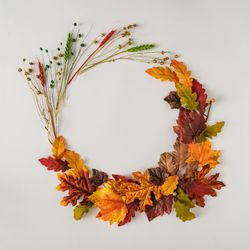 Autumn branches and leaves arranged in festive wreath on light background