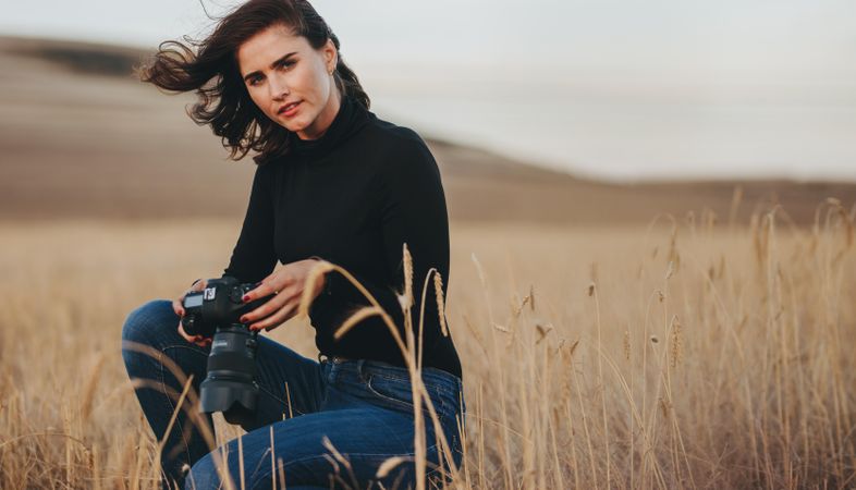 Woman photographer with camera crouching in a dry grass field