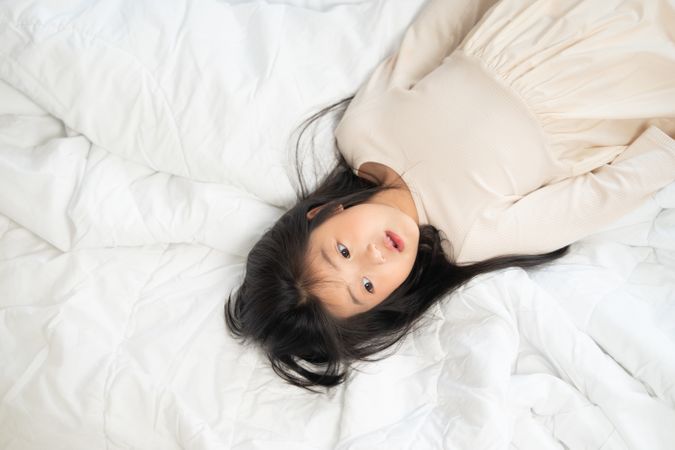Asian happy girl in white dress lying on bed.