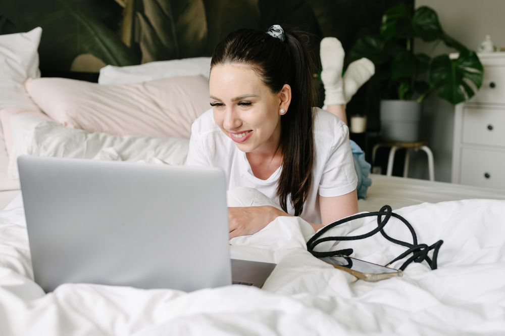 Smiling woman using laptop in bed during weekend