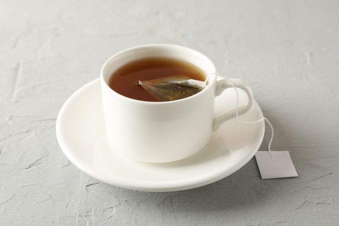 Cup of tea with tea bag on grey background, close up
