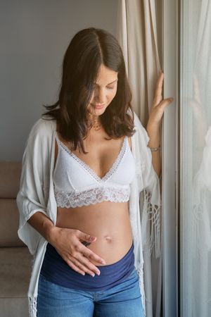 Brunette standing near window in living room during pregnancy