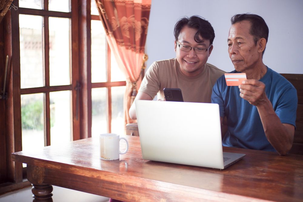 Happy adult son and old father pay online using laptop and credit card