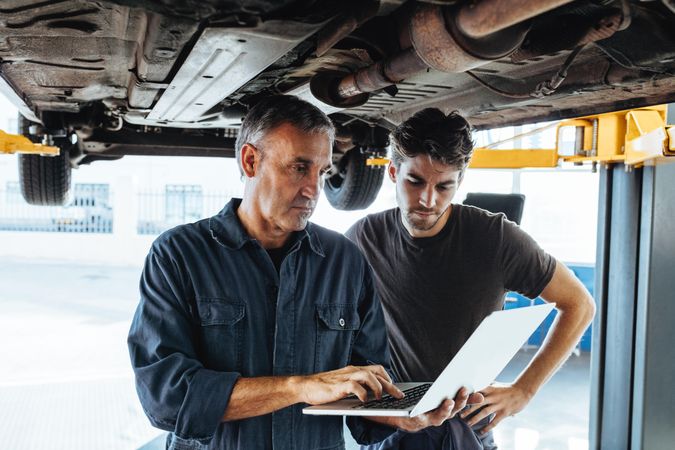 Auto service professionals using laptop while examining the car