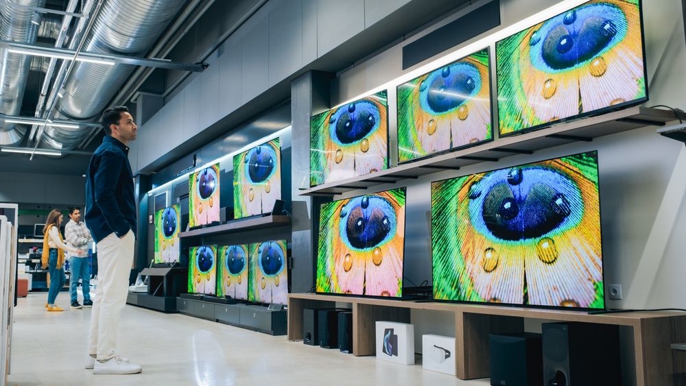 Portrait of a Stylish Man Looking at a Variety of Modern Smart TV Sets with High Quality Resolution Displays and Vivid Color Transmission.