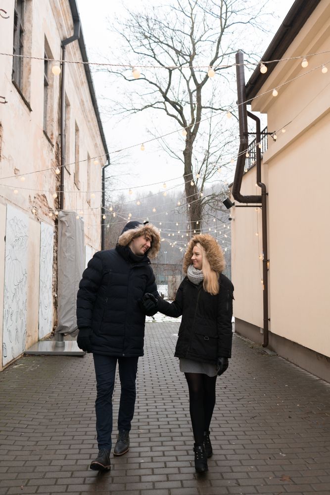 Smiling couple holding hands on street with fairy lights hanging on buildings